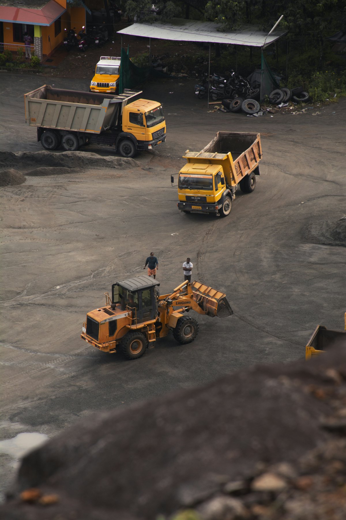Aerial view of a working yard: dump trucks and a wheel loader moving aggregate.